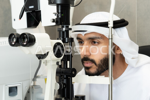 تقييم مدى الرؤية والكشف عن الامراض العينية ، مفهوم الخدمات والرعاية الصحية في المشافي والمراكز الطبية، استخدام الأجهزة الحديثة المتطورة، رجل عربي خليجي اماراتي يقوم بفحص عينيه بجهاز المنظار العيني، تشخيص وتحديد المشاكل البصرية، التأكد من صحة البصر