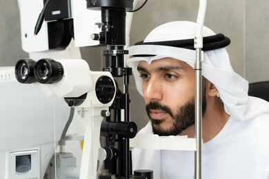 تقييم مدى الرؤية والكشف عن الامراض العينية ، مفهوم الخدمات والرعاية الصحية في المشافي والمراكز الطبية، استخدام الأجهزة الحديثة المتطورة، رجل عربي خليجي اماراتي يقوم بفحص عينيه بجهاز المنظار العيني، تشخيص وتحديد المشاكل البصرية، التأكد من صحة البصر