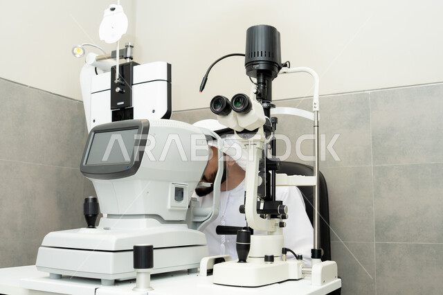 Ensuring the accuracy of vision, assessing the extent of vision and detecting eye diseases, the concept of services and healthcare in hospitals and medical centers, an Arab Gulf Emirati man examining his eyes with an ophthalmoscope, diagnosing and identifying visual problems, using advanced modern devices.