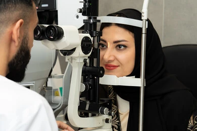 Assessment of visual acuity and detection of eye diseases, the concept of services and healthcare in hospitals and medical centers, diagnosis and identification of visual problems, use of advanced modern devices, an Emirati Gulf Arab doctor examining the eyes of an Emirati woman with an ophthalmoscope.