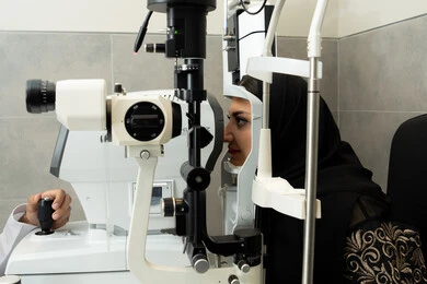 A Saudi woman is checking her vision health, assessing visual acuity and detecting eye diseases, diagnosing and identifying visual problems, using advanced modern devices. An Arab Gulf Emirati woman is examining her eyes with an ophthalmoscope, the concept of health services and care in hospitals and medical centers.