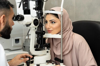 The concept of healthcare services in hospitals and medical centers, diagnosing and identifying visual problems, using advanced modern devices, an Arab Gulf Emirati doctor examining the eyes of an Emirati woman with an ophthalmoscope, assessing the level of vision and detecting eye diseases.