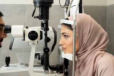The use of advanced modern devices, diagnosing and identifying visual problems, an Arab Gulf Emirati doctor examining the eyes of an Emirati woman with an ophthalmoscope, assessing the extent of vision and detecting eye diseases, the concept of health services and care in hospitals and medical centers.