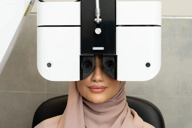 Diagnosis and identification of visual problems, assessment of vision and detection of eye diseases, a Saudi woman using advanced modern devices, an Arab Gulf Emirati woman wearing an abaya in front of an eye examination machine to ensure the health of her vision, the concept of health services and care in hospitals and centers.