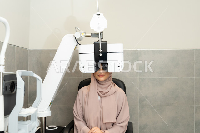 Assessment of vision and detection of eye diseases, a Saudi woman using advanced modern devices, diagnosing and identifying visual problems, a Gulf Arab Emirati woman wearing an abaya in front of an eye examination device to ensure eye health, the concept of health services and care in hospitals and centers.