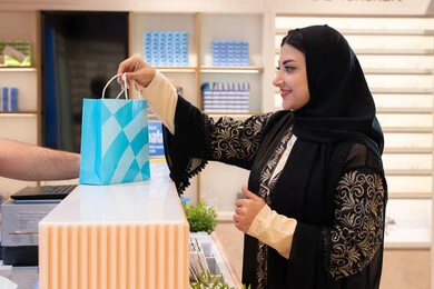 Following the latest trends in fashion and beauty, a Saudi woman is buying sunglasses, an Arab Gulf Emirati woman in an Emirati store, the concept of shopping and browsing from the mall, acquiring the latest modern stylish eyewear products.