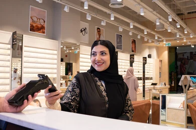 اقتناء الهدايا من احدي المولات الاماراتيه، تطبيقات الشراء الالكتروني عبر الهاتف،امراة عربيه خليجيه اماراتية ترتدي العباءه السوداء تقوم بعملية الدفع باستخدام الهاتف المحمول ،ايماءات السعاده و السرور ، سيدة سعودية تقوم بالتسوق والتبضع