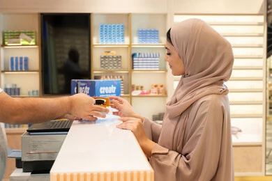 Attention to appearance, elegance, and fashion, buying glasses to protect the eyes from rays, an Arab Gulf Emirati woman wearing a colorful abaya is buying suitable sunglasses in an Emirati store with gestures of happiness and joy, a Saudi woman is shopping and browsing.