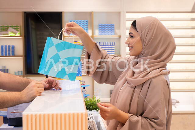 Acquiring gifts from one of the Emirati malls, an Arab Gulf woman from the UAE wearing a colorful abaya is holding a colorful paper bag with gestures of happiness and joy, a Saudi woman is shopping and doing her shopping.