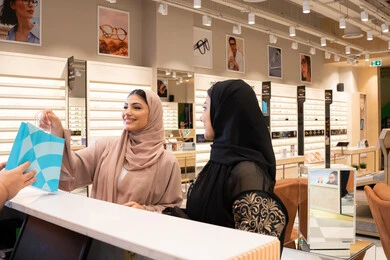 The concept of shopping and buying from the mall, acquiring the latest trendy eyewear products, two Emirati Gulf Arab friends in an Emirati store, an Emirati woman buying sunglasses, following the latest fashion and beauty trends.