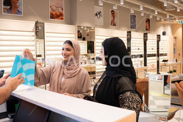 اقتناء أحدث منتجات النظارات العصرية الحديثة, صديقتان عربيان خليجيان اماراتيان في متجر اماراتي, امراة اماراتيه تقوم بشراء نظارة شمسية، مفهوم التسوق و التبضع من المول ، متابعة آخر صيحات الموضة والجمال