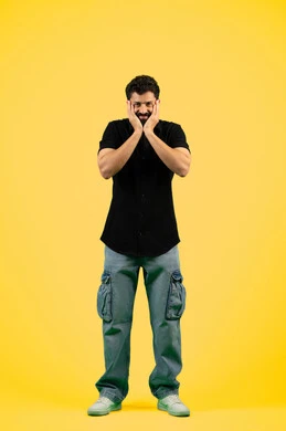 Receiving unexpected happy news, a young Emirati man looking at the camera with gestures of shock, wonder and amazement, being surprised by a specific situation, feeling astonished and amazed, remembering something, portrait of a Saudi Arabian Gulf man wearing casual summer clothes and putting his hands on his face, full body photo, yellow background