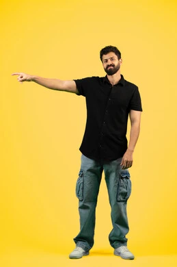 The concept of elegance and interest in outward appearance, portrait of a smiling young Arab Gulf Emirati man wearing casual clothes, standing straight and looking at the camera with self-confident gestures, a Saudi man pointing his index finger at something, full body, yellow background