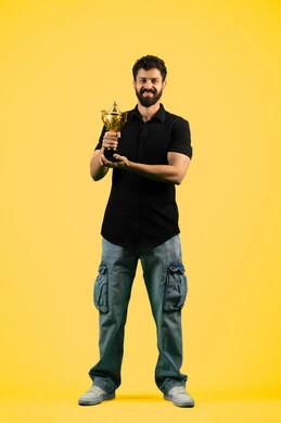 تشجيع الأنديه والمنتخبات، أنشطة ترفيهية ممتعة، شاب سعودي ينظر إلى الكاميرا بإيماءات الفرح والسعادة لفوز الفريق المفضل، رجل عربي خليجي اماراتي مبتسم يرتدي الزي الكاجوال يمسك بيده الكأس الذهبي، صورة الجسم بالكامل، خلفية صفراء