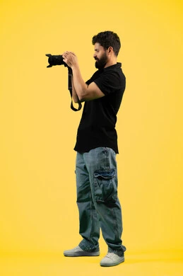 Mastering photography using high-resolution digital cameras, a professional Saudi photographer taking souvenir photos, practicing the hobby of photography with happy expressions, a portrait of a young Arab Gulf Emirati man wearing casual clothes holding a camera, a full body photo, a yellow background