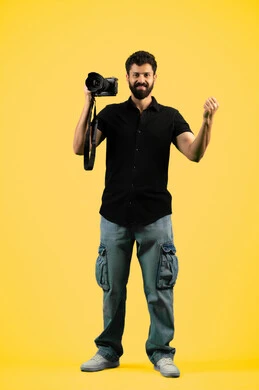 Mastering photography using high-resolution digital cameras, a professional Saudi photographer taking souvenir photos, raising his fist with gestures of joy and victory, a portrait of a young Arab Gulf Emirati man wearing casual clothes holding a camera, full body photo, yellow background