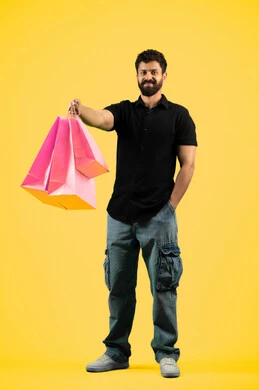 Shopping and taking the necessary needs, taking advantage of the discount and clearance seasons, commercial purchases and gifts, a young Saudi man looking at the camera with an expression of pleasure, a portrait of an Arab Gulf Emirati man wearing casual clothes and holding paper bags in his hand, a full body photo, a yellow background