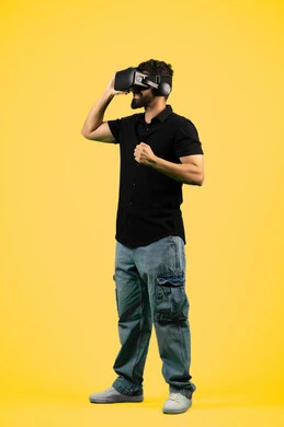 المتعة بمشاهدة الأفلام ومحاكاة العالم الخيالي, بورتريه لشاب عربي سعودي خليجي يرتدي الزي الكاجوال ونظارة في آر ثلاثية الأبعاد, التفاعل والاندماج مع ألعاب الواقع الافتراضي,  رجل اماراتي يرفع قبضة يده لمحاولة إمساك شيء ما، صورة الجسم بالطول الكامل، خلفية صفراء