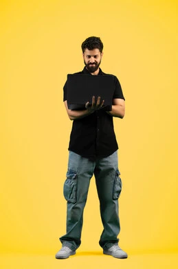 Browsing social media, watching movies and TV series, portrait of a young Saudi Arabian Gulf man wearing casual clothes holding a laptop, the concept of hard work and completing required tasks, an Emirati man looking at a computer, full body, yellow background