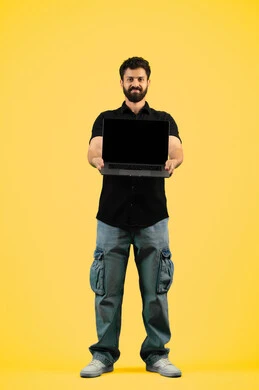 استخدام الأجهزة الحديثة في انجاز المهام, بورتريه لرجل عربي خليجي اماراتي يرتدي الزي الكاجوال يحمل الحاسوب المحمول، شاب سعودي يعرض شاشة سوداء فارغة عبر اللابتوب، الجسم بالطول الكامل، خلفيه صفراء