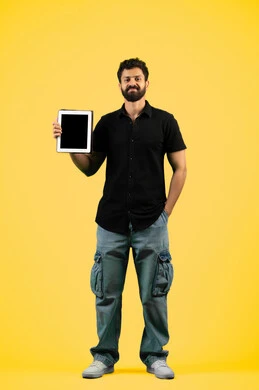 النظر إلى الكاميرا بإيماءات السعادة، استخدام التكنولوجيا الحديثة والمتطورة، شاب سعودي يعرض شاشة سوداء فارغة عبر الجهاز اللوحي، بورتريه لرجل عربي خليجي اماراتي يرتدي الزي الكاجوال يمسك بيده التابلت المحمول، طول الجسم بالكامل، خلفية صفراء