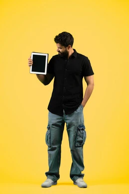 Using modern and advanced technology, a young Saudi man displays a blank black screen on a tablet, portrait of an Arab Gulf Emirati man wearing casual clothes holding a tablet in his hand, full body length, yellow background