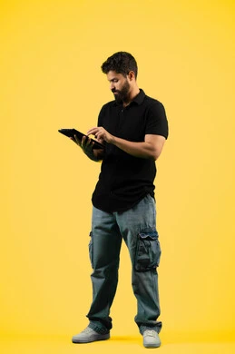 Using a tablet to complete work tasks, a Saudi young man browsing social media applications, using modern and advanced technology, a portrait of an Arab Gulf Emirati man wearing casual clothes using a tablet with focus gestures, full body length, yellow background