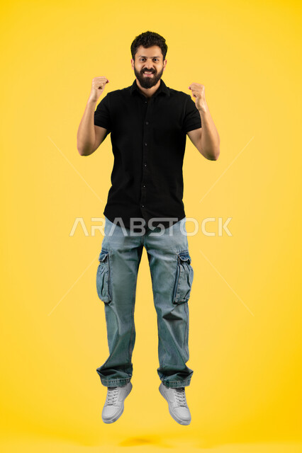 Mastering boxing, increasing muscle endurance, portrait of a smiling young Arab Gulf Emirati man in casual wear raising his fists with power gestures, Saudi man looking at the camera with a confident expression, practicing self-defense, full body image, yellow background