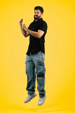 إتقان فنون الملاكمة، زيادة قدرة العضلات على التحمل، بورتريه لشاب عربي خليجي اماراتي مبتسم يرتدي الزي الكاجوال يرفع قبضات يديه بإيماءات القوة، رجل سعودي ينظر إلى الكاميرا بتعابير الثقة بالنفس، ممارسة رياضة الدفاع عن النفس، صورة الجسم بالطول الكامل، خلفية صفراء