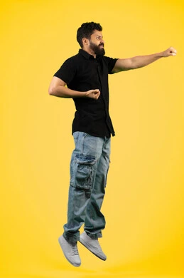 ممارسة رياضة الدفاع عن النفس، إتقان فنون الملاكمة، زيادة قدرة العضلات على التحمل، بورتريه من الجانب لشاب عربي خليجي اماراتي مبتسم يرتدي الزي الكاجوال يرفع قبضات يديه بإيماءات القوة، رجل سعودي ينظر إلى الكاميرا بتعابير الثقة بالنفس، الجسم بالطول الكامل، خلفية صفراء