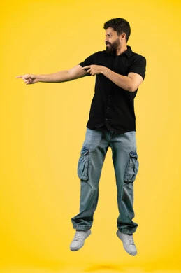 Pointing to something specific, elegance and interest in outward appearance, portrait of a smiling young Arab Gulf Emirati man wearing casual clothes standing straight, Saudi man pointing with his index finger at something, full body, yellow background