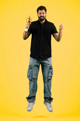 Fun recreational activities, a young Saudi man looking at the camera with gestures of joy and happiness for his favorite team's victory, cheering for clubs and national teams, a smiling Emirati Gulf Arab man wearing casual clothes holding the golden cup in his hand, raising his fist with expressions of victory and enthusiasm, full body image, yellow background
