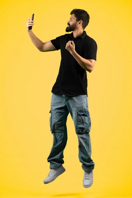 Live broadcast on social media, raising fist in victory gesture, portrait of Saudi man in casual clothes taking souvenir photos with mobile phone, Arab Emirati Gulf man answering a video call, full body shot, yellow background