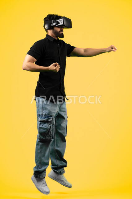 Enjoy watching movies and simulating the imaginary world, portrait of a young Saudi Arabian Gulf man wearing casual clothes and 3D VR glasses, interacting and immersing himself in virtual reality games, Emirati man raising his fists with boxing gestures, full-length body image, yellow background