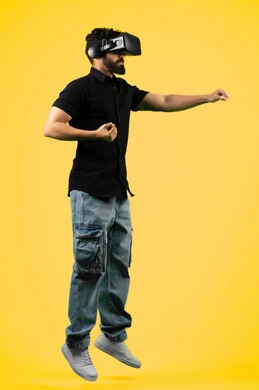 الاستمتاع بمشاهدة الأفلام ومحاكاة العالم الخيالي, بورتريه لشاب عربي سعودي خليجي يرتدي الزي الكاجوال ونظارة في آر ثلاثية الأبعاد, التفاعل والاندماج مع ألعاب الواقع الافتراضي,  رجل اماراتي يرفع قبضة يديه بإيماءات الملاكمة، صورة الجسم بالطول الكامل، خلفية صفراء