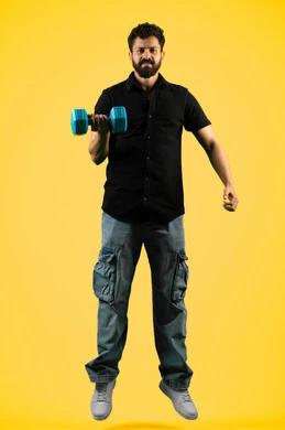 Looking at the camera with a confident expression, physical activity to maintain health and fitness, Emirati young man practicing weightlifting (dumbbells), burning fat and calories, portrait of a Saudi Arabian Gulf man wearing casual clothes holding iron weights, full body, yellow background