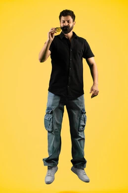 استخدام العدسات الطبية الملونة لحماية العين من أشعة الشمس، اقتناء نظارات جديدة، الأناقة والوسامة والاهتمام بالمظهر الخارجي، بورتريه لرجل عربي خليجي اماراتي  يرتدي الزي الكاجوال يحمل نظارة شمسية سوداء، القفز عاليا بتعابير السعادة، الجسم بالطول الكامل, خلفية صفراء