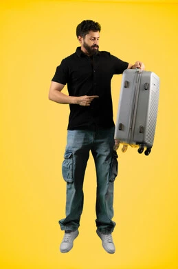 مفهوم السياحة والسفر، جولات ترفيهية في إجازة الصيف, بورتريه لشاب عربي خليجي اماراتي مبتسم يرتدي الزي الكاجوال يحمل حقيبة السفر ويشير بإصبع السبابة إليها, رجل سعودي يستعد لقضاء رحلة صيفية ممتعة, صورة الجسم بالطول الكامل، خلفية صفراء