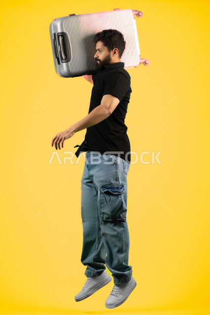 Summer vacation leisure tours, portrait of a smiling young Arab Emirati man in casual wear carrying a suitcase, tourism and travel concept, Saudi man preparing for a fun summer trip, full body image, yellow background