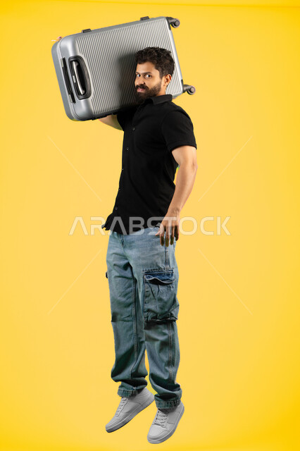 جولات ترفيهية في إجازة الصيف, بورتريه لشاب عربي خليجي اماراتي مبتسم يرتدي الزي الكاجوال يحمل حقيبة السفر, مفهوم السياحة والسفر، رجل سعودي يستعد لقضاء رحلة صيفية ممتعة, صورة الجسم بالطول الكامل، خلفية صفراء