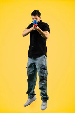 The concept of entertainment and amusement, having a good time with water games in the summer, a portrait of a young Arab Gulf Emirati man wearing casual clothes holding a plastic water gun playing with gestures of pleasure and happiness, full body, braided background