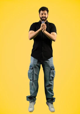 الفن المسرحي الغنائي، مواهب فنية في عالم الموسيقى، تقديم العروضات المسرحية، رجل اماراتي يقوم بممارسة هواية الغناء للتسلية والترفيه، بورتريه لشاب عربي سعودي خليجي يرتدي الزي الكاجوال يحمل بيده الميكروفون، طول الجسم بالكامل، خلفية صفراء