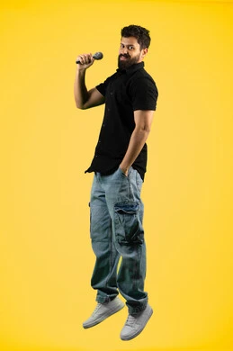 مواهب فنية في عالم الموسيقى، الغناء بحماس وصوت عالي، الفن المسرحي الغنائي، تقديم العروضات المسرحية، رجل اماراتي يقوم بممارسة هواية الغناء للتسلية والترفيه، بورتريه لشاب عربي سعودي خليجي يرتدي الزي الكاجوال يحمل بيده الميكروفون، طول الجسم بالكامل، خلفية صفراء