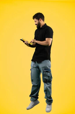 Using a tablet to complete work tasks, a Saudi young man browsing social media applications, using modern and advanced technology, a portrait of an Arab Gulf Emirati man wearing casual clothes using a tablet with focus gestures, full body length, yellow background