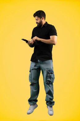 Using modern and advanced technology, using a tablet to complete work tasks, a Saudi young man browsing social media applications, a portrait of an Arab Gulf Emirati man wearing casual clothes writing with a pen on a tablet with focus gestures, full body length, yellow background