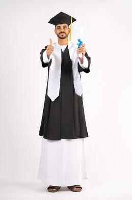 Thumbs up gesture, occasion and joy of success, taking selfies in graduation gown, celebrating the completion of university, portrait of a young Arab Gulf Emirati graduate wearing a graduation cap and gown holding a certificate looking at the camera with gestures of pleasure, white background