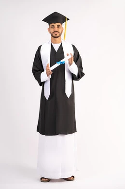 إنهاء المرحلة الجامعية، تعابير السرور والسعادة بالنجاح، التقاط صور شخصية بثياب التخرج، بورتريه لشاب خريج عربي خليجي اماراتي مبتسم يرتدي القبعة وعباءة التخرج يحمل الشهادة ينظر الى الكاميرا بإيماءات البهجة، الجسم بالطول الكامل، خلفية بيضاء