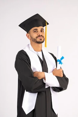 التقاط صور شخصية بثياب التخرج، الاحتفال بإنهاء المرحلة الجامعية، بورتريه لشاب خريج عربي خليجي اماراتي مبتسم يرتدي القبعة وعباءة التخرج يقف بأيدي متقاطعة ينظر الى الكاميرا بتعابير الثقة بالنفس، مفهوم التفوق والنجاح والاجتهاد، خلفية بيضاء