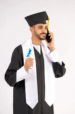 التواصل مع الأهل والأصدقاء، مفهوم الاجتهاد والتفوق، الاحتفال بإنهاء الدراسة الجامعية، استخدام التقنية الحديثة، بورتريه مقرب لشاب خريج عربي خليجي اماراتي يرتدي عباءه وقبعة التخرج يقوم بإجراء مكالمة عبر الهاتف المحمول،  خلفية بيضاء