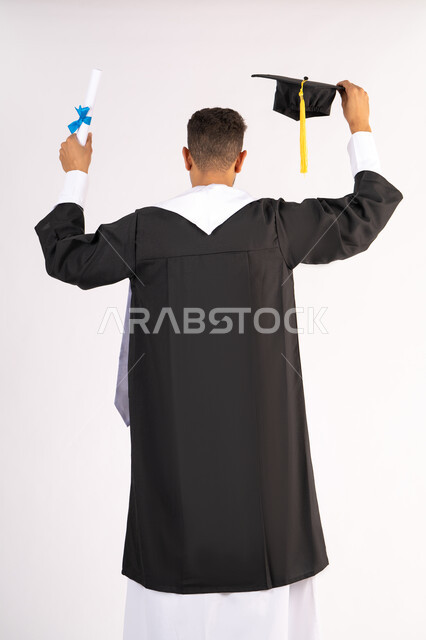 Quality of education in the United Arab Emirates, feeling proud and happy to achieve the dream of graduation, portrait from the back of a young Emirati Gulf Arab graduate wearing an abaya raising the graduation cap and certificate, celebrating the completion of the university stage, white background